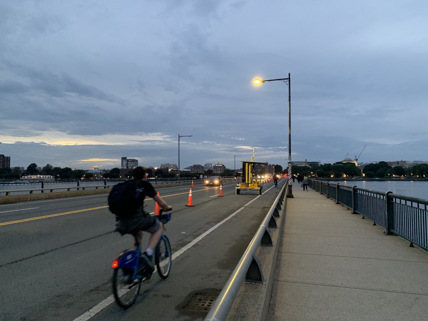 A biker zooming across the Harvard bridge. Bits of orange peek out from blue-gray sky and the street lamps feel beautifully warm.