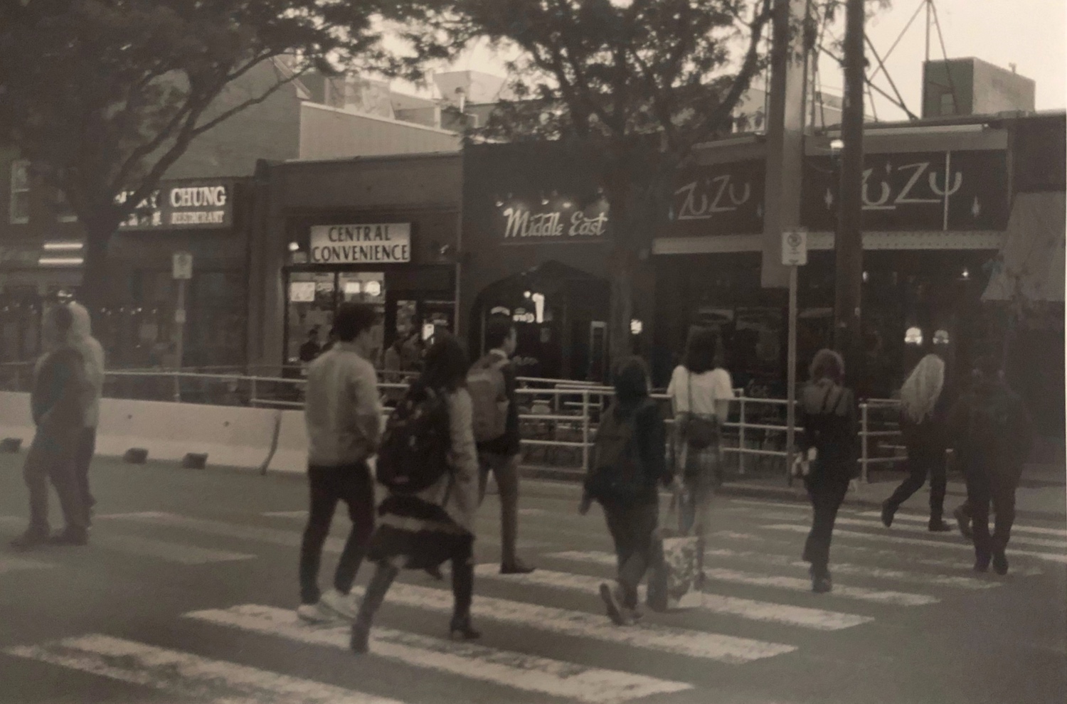 A black and white film photo of people crossing the street. It's the beatles but from the back but they're just as cool.