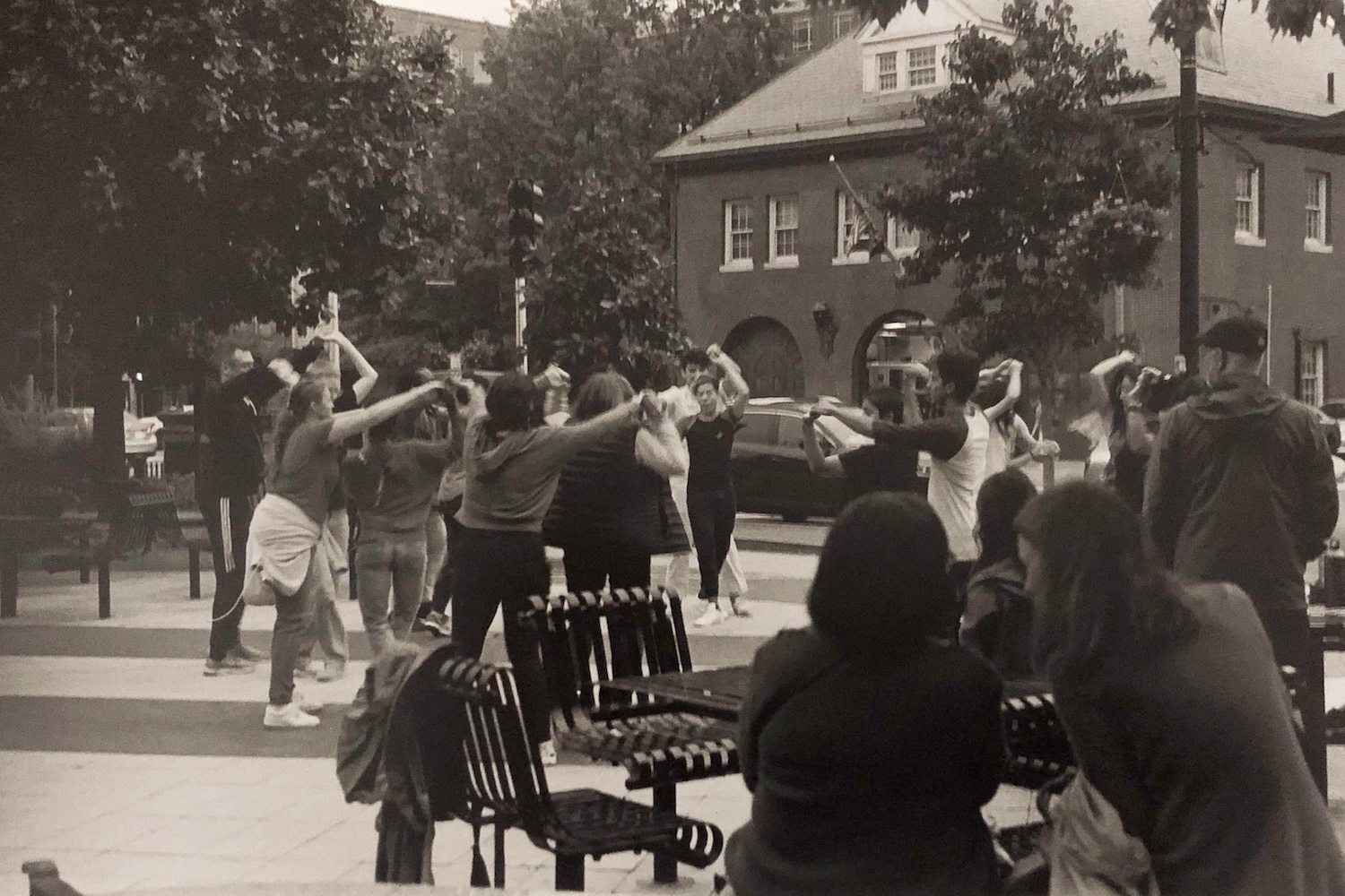 A black and white film photo of people casually salsa dancing in the middle of the square, the sun in their steps and ice cream in the air.
