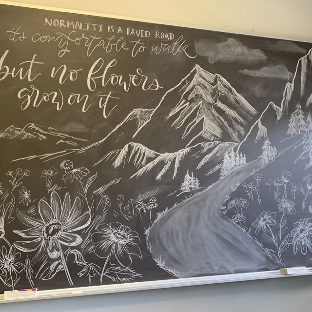 chalkboard drawing of flowers in a field with mountains in the background