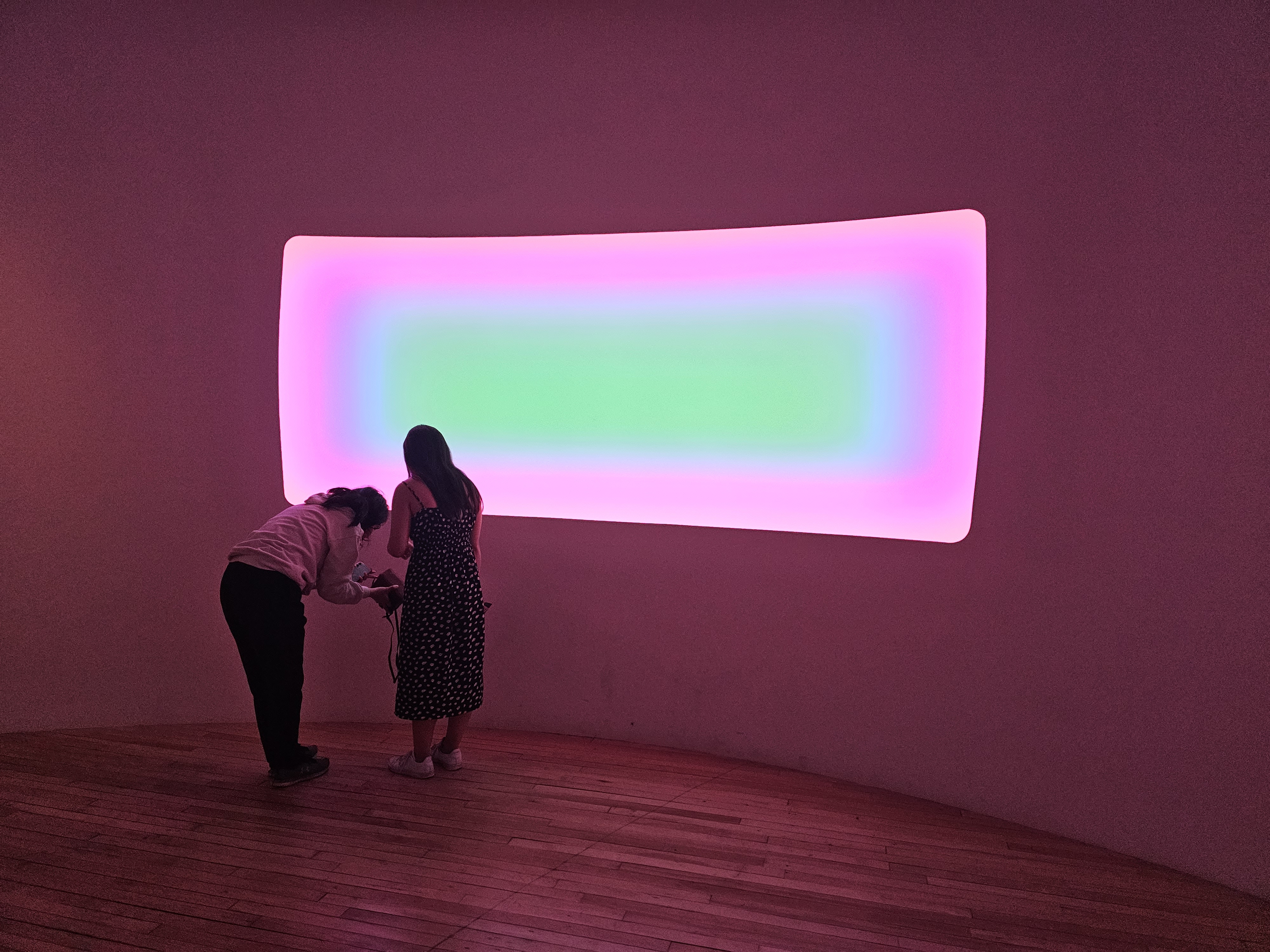 two people standing in front of a glowing rainbow wall
